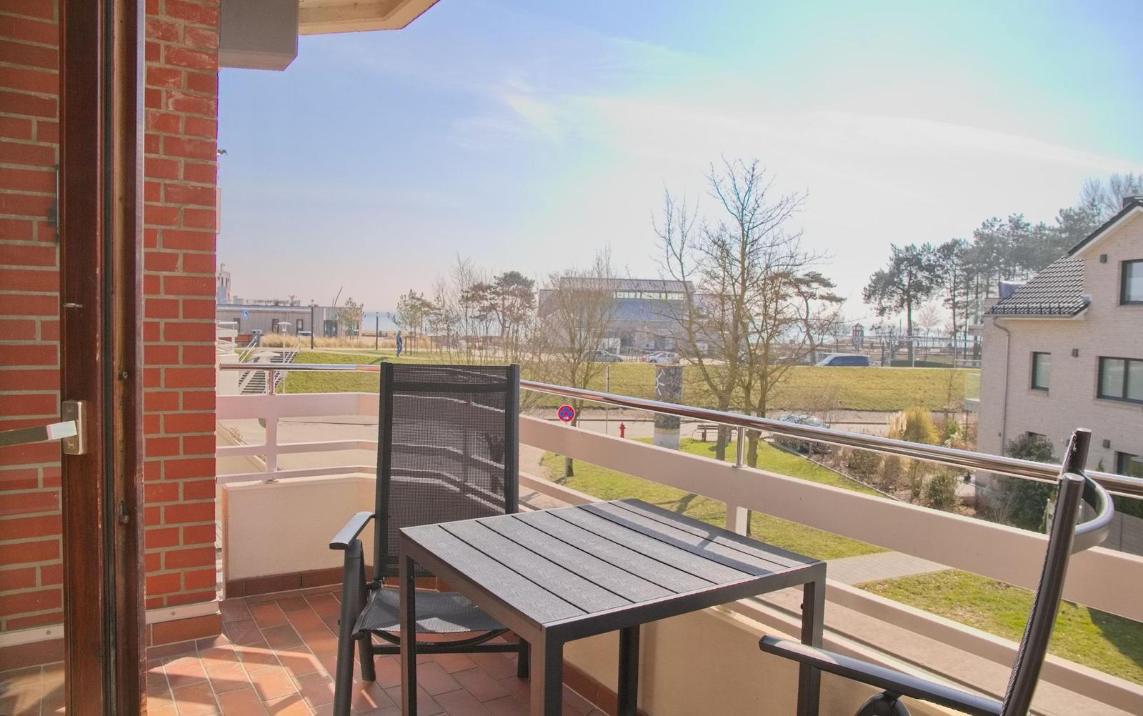 Terrasse mit Tisch und Stühlen, Blick auf Grünfläche und Gebäude.