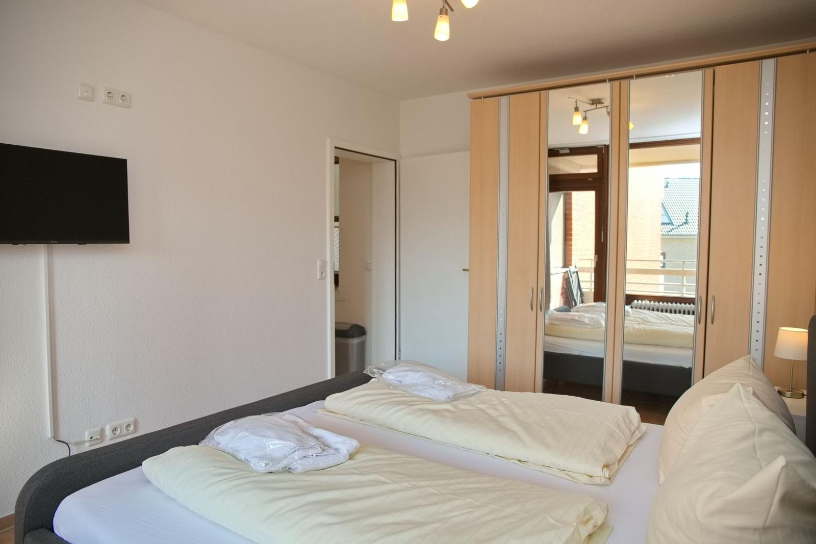 Schlafzimmer mit Doppelbett, Spiegelschrank und Fernseher an der Wand.