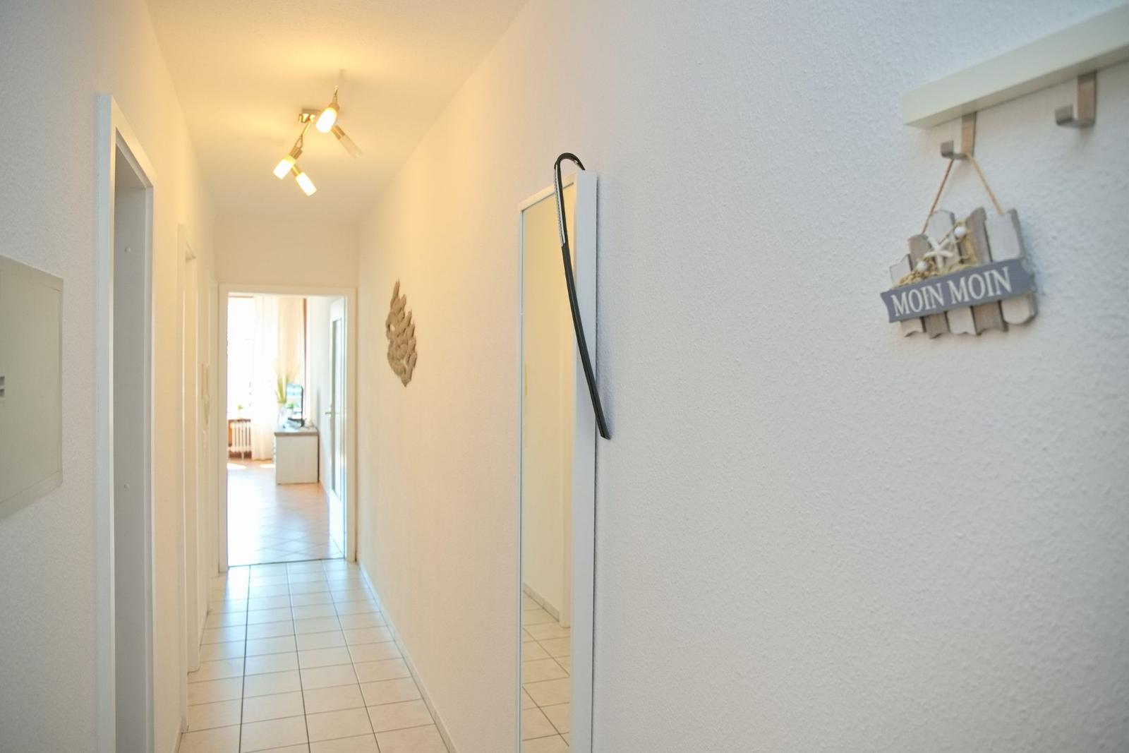 Flur mit weißen Wänden, Fliesenboden und Türöffnungen. An der Wand hängt ein Schild mit MOIN MOIN.