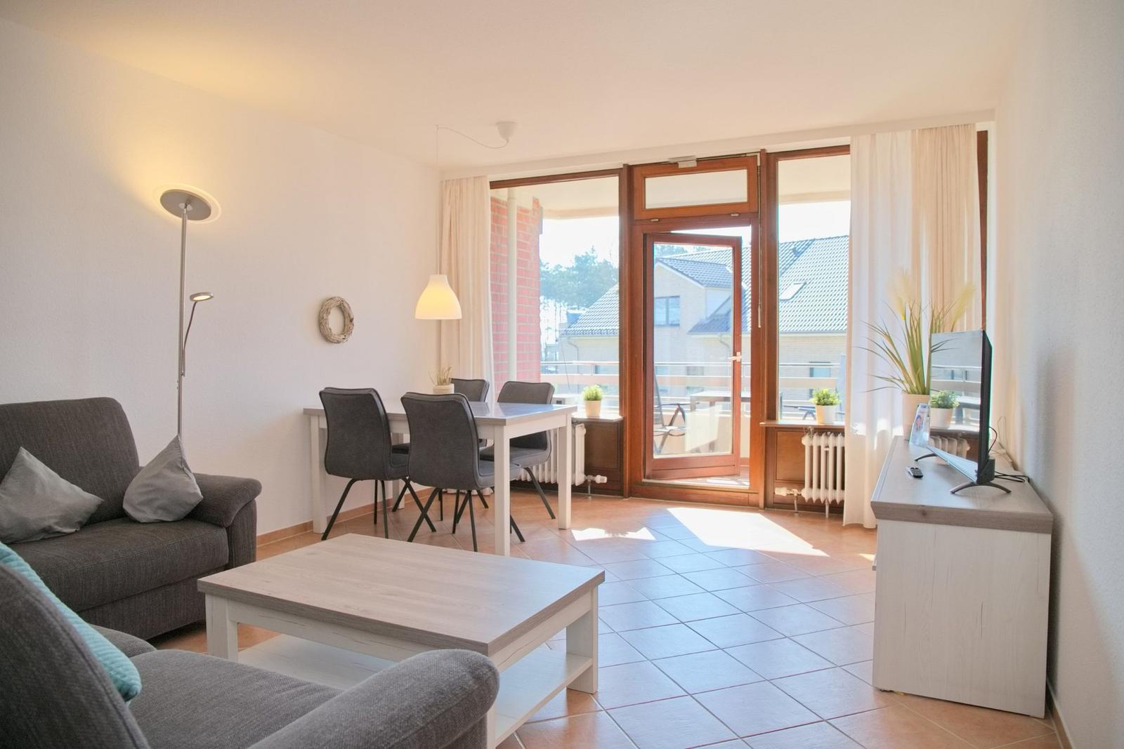 Wohn- und Essbereich mit Balkontür, Sofa, Tisch und Fernseher.