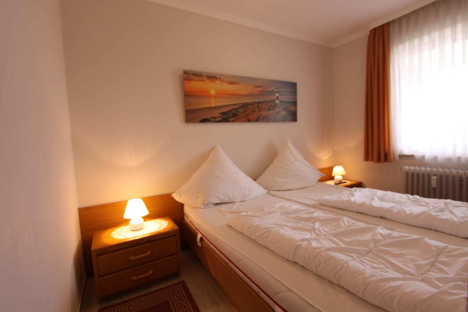 Schlafzimmer mit Doppelbett, Nachttisch und Wandbild. Fenster mit Vorhängen.