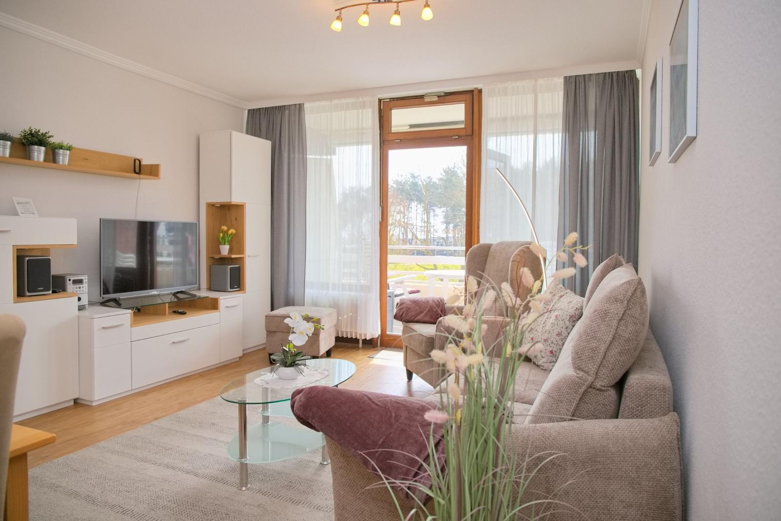 Wohnzimmer mit Sofa, Fernseher und Balkonansicht.