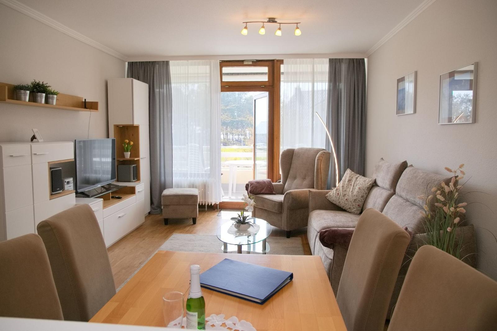 Wohnzimmer mit Sofa, Sessel und Esstisch. Balkon mit Blick nach draußen.