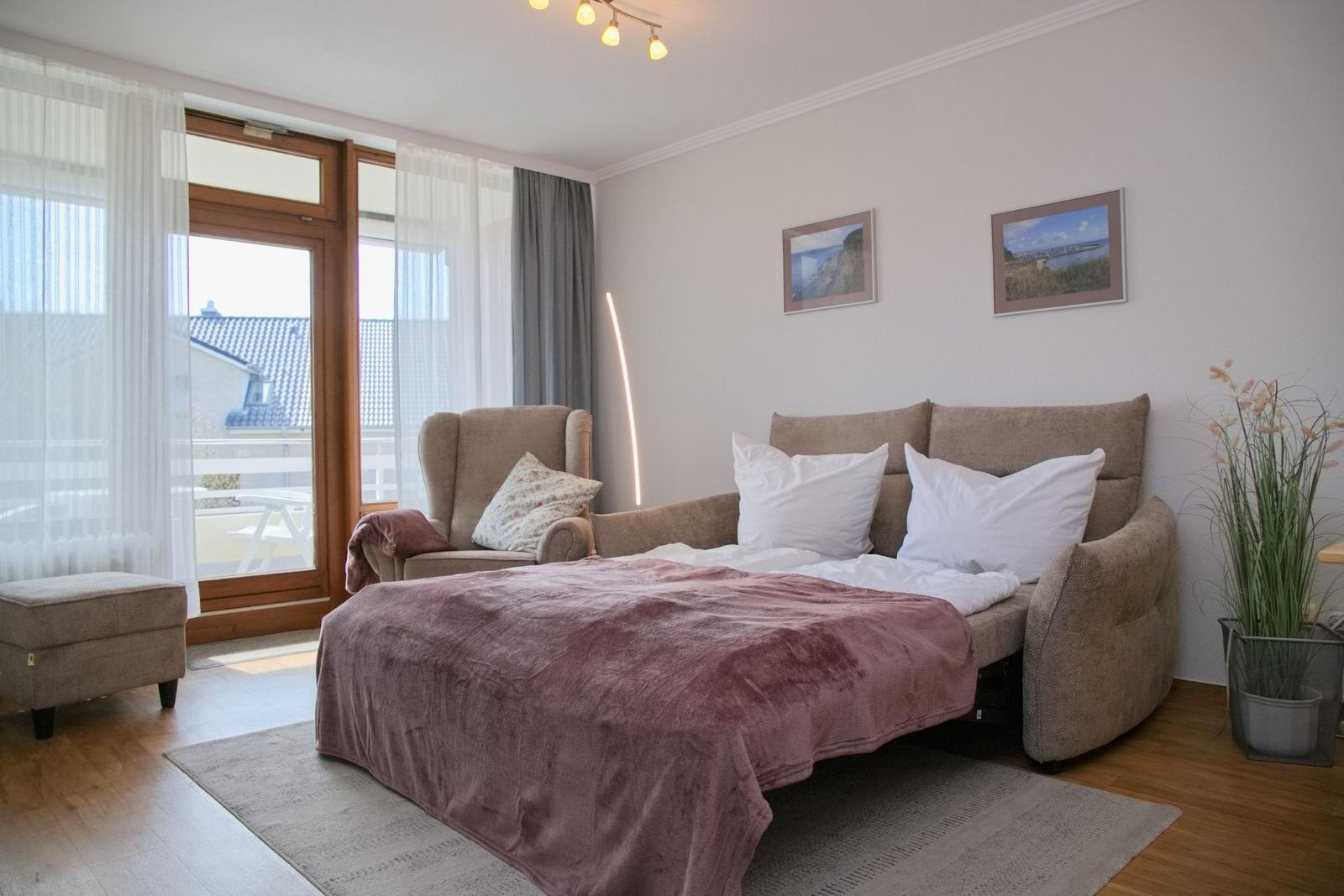 Ein Schlafzimmer mit Bett, Sessel und Fenster zur Terrasse.