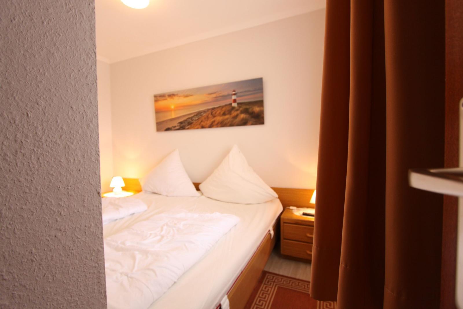 Schlafzimmer mit Bett, Nachttisch und Wandbild mit Leuchtturm.