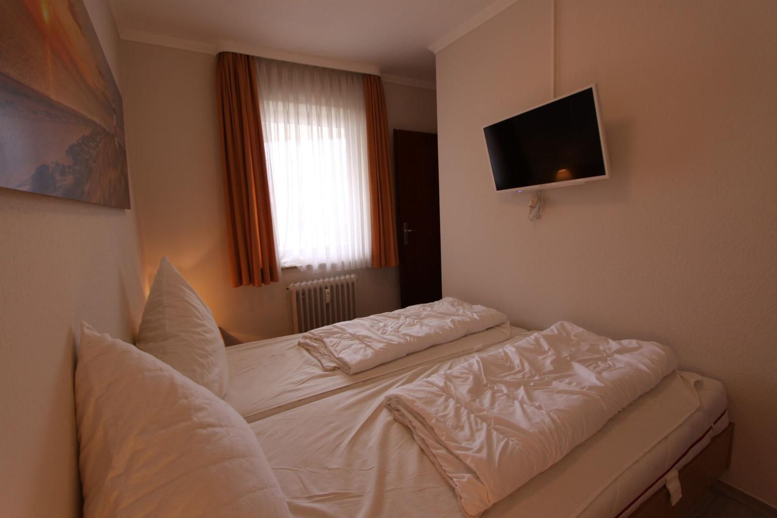 Schlafzimmer mit Doppelbett, Wandfernseher und Fenster mit Vorhängen.