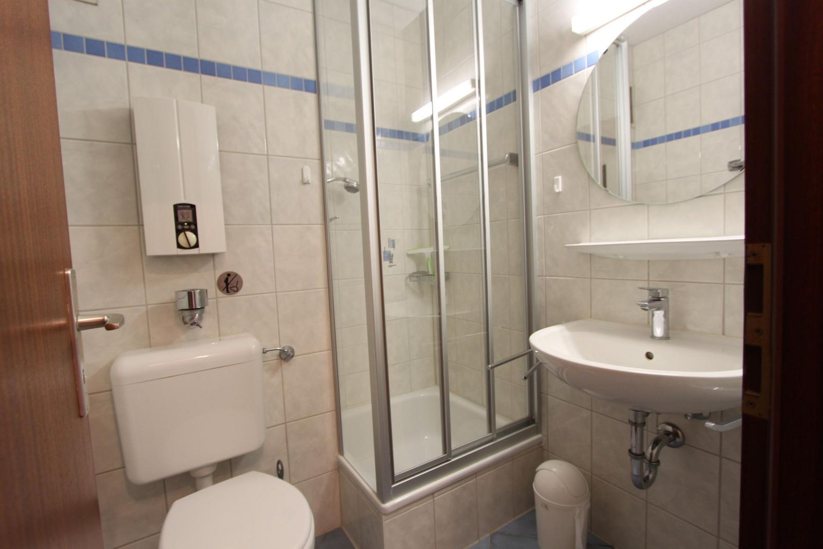Badezimmer mit Dusche, Waschbecken und Toilette. Fliesen mit blauer Bordüre.