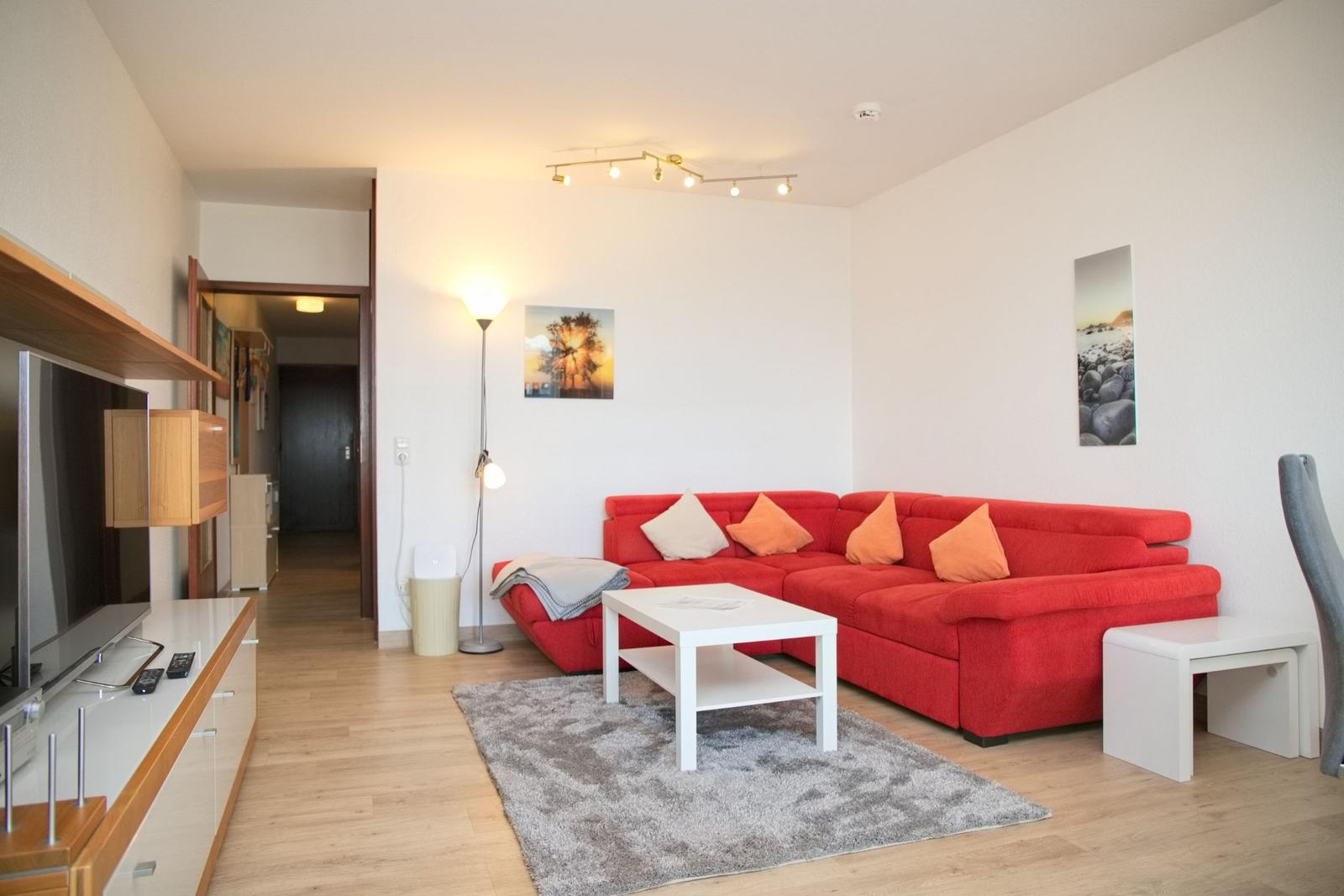 Wohnzimmer mit rotem Sofa, weißem Couchtisch und Holzboden.