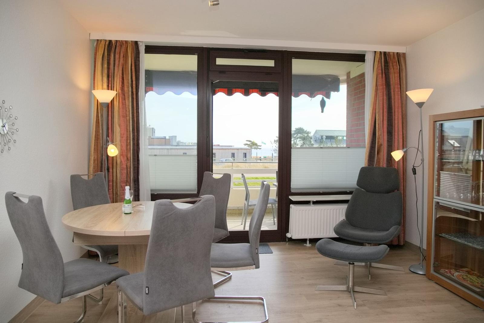 Essbereich mit runder Tisch und Stühlen, Sessel und Blick auf Balkon.
