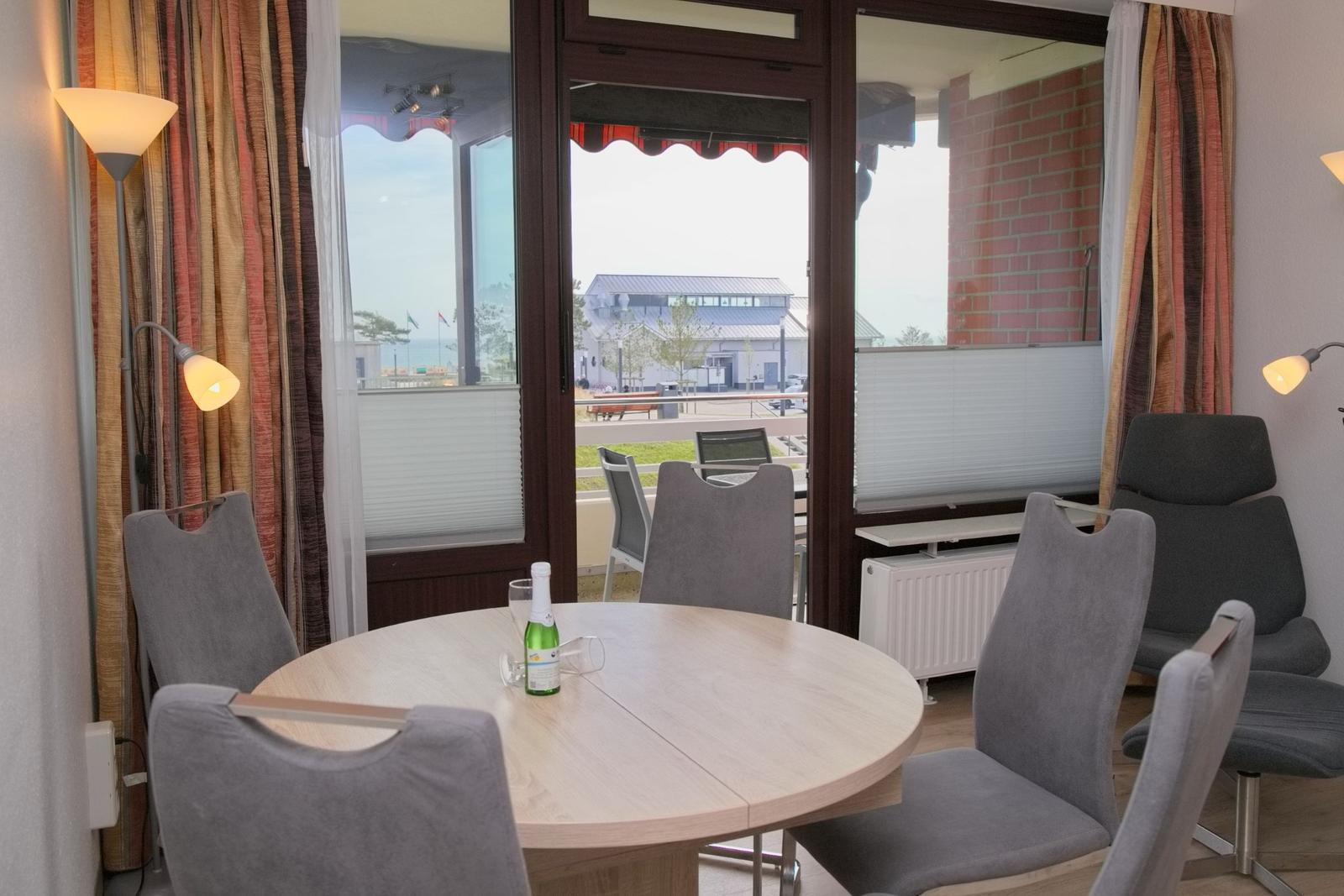 Runde Tisch mit Stühlen und Blick auf Balkon. Vorhänge und Lampe sichtbar.