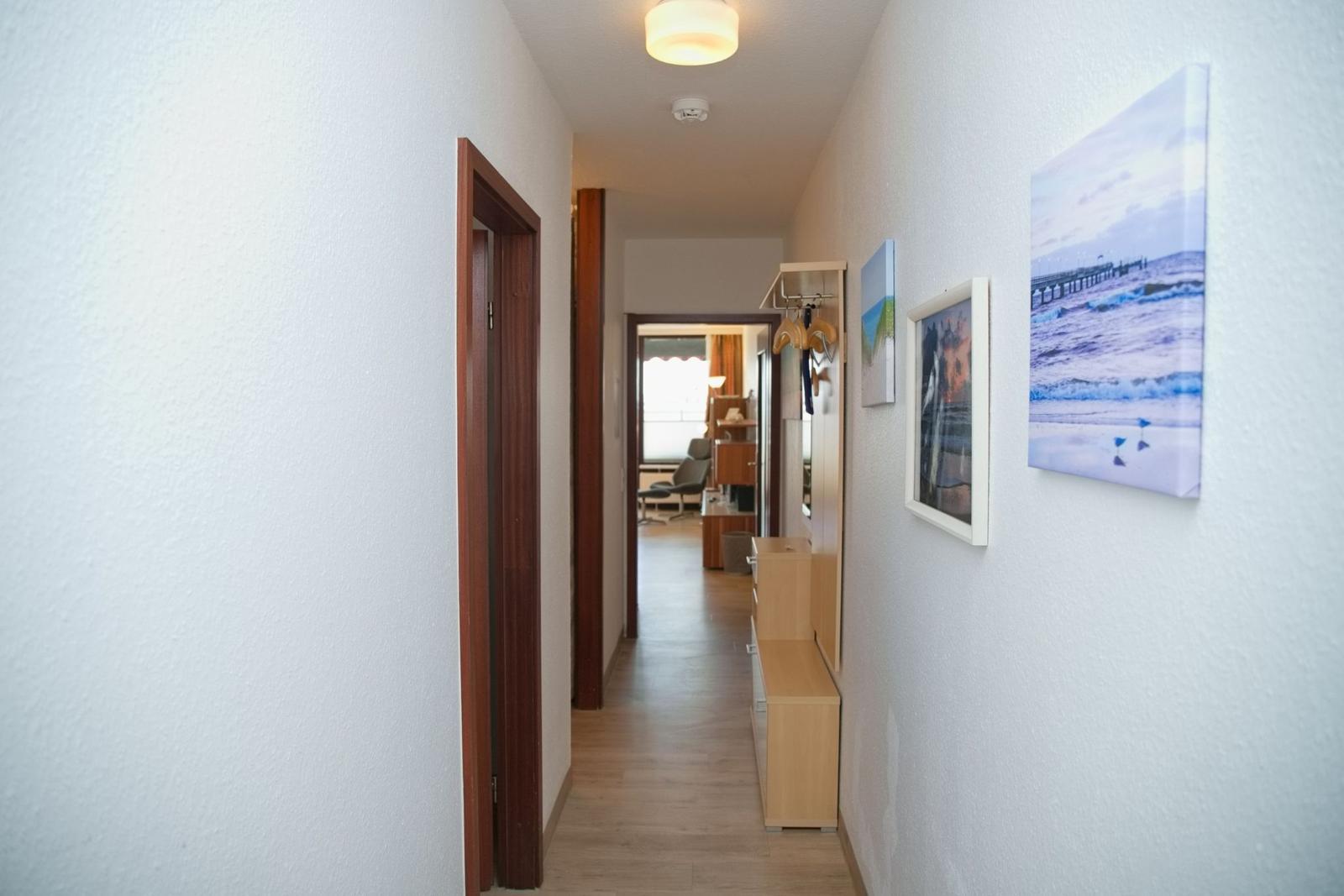 Flur mit Bildern an der Wand und Blick in Wohnbereich.