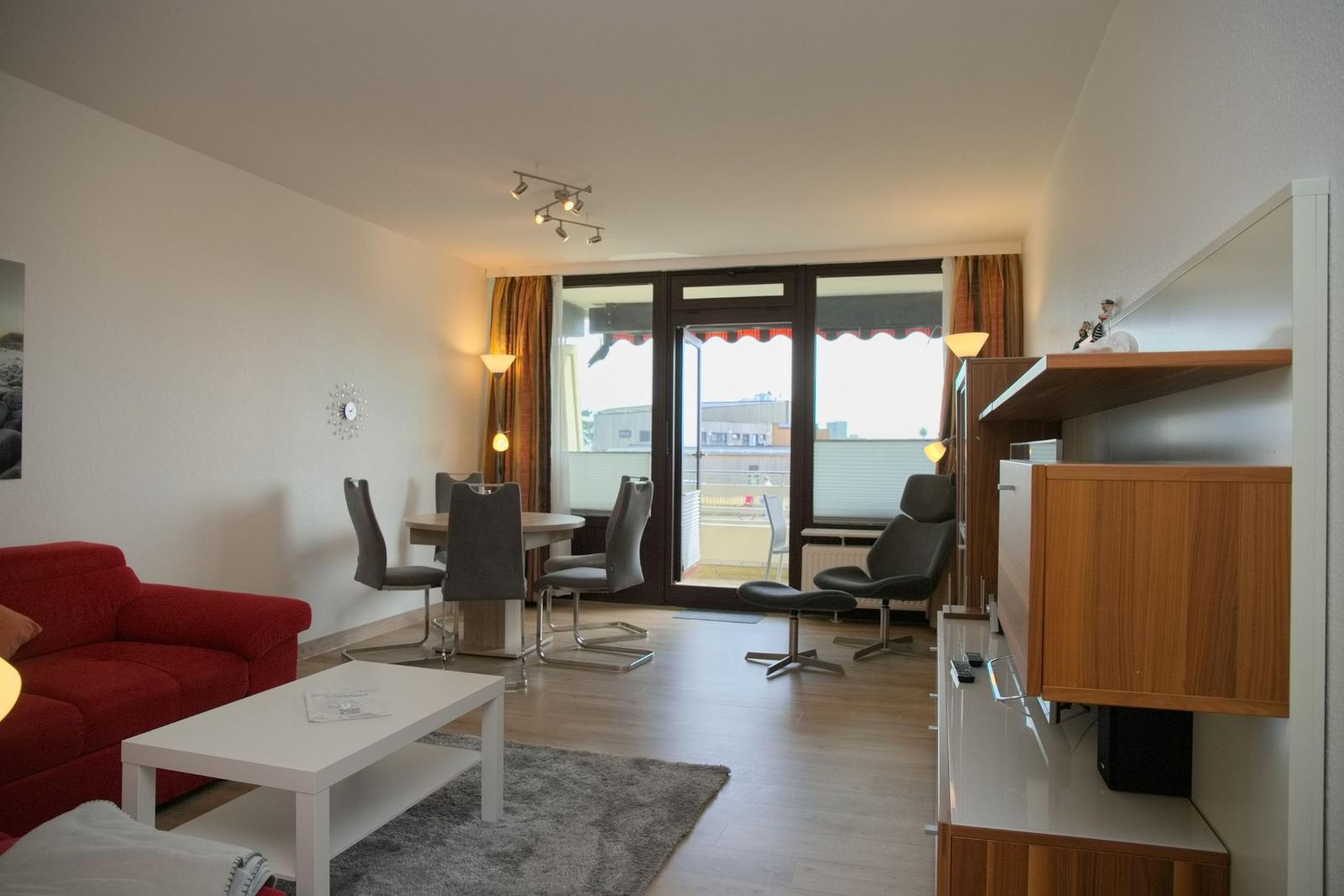 Wohnzimmer mit rotem Sofa, Esstisch und Balkonzugang.
