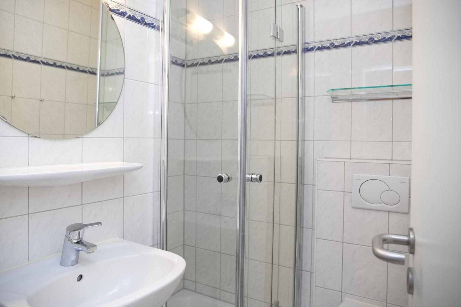 Badezimmer mit Dusche, Waschbecken und Spiegel.