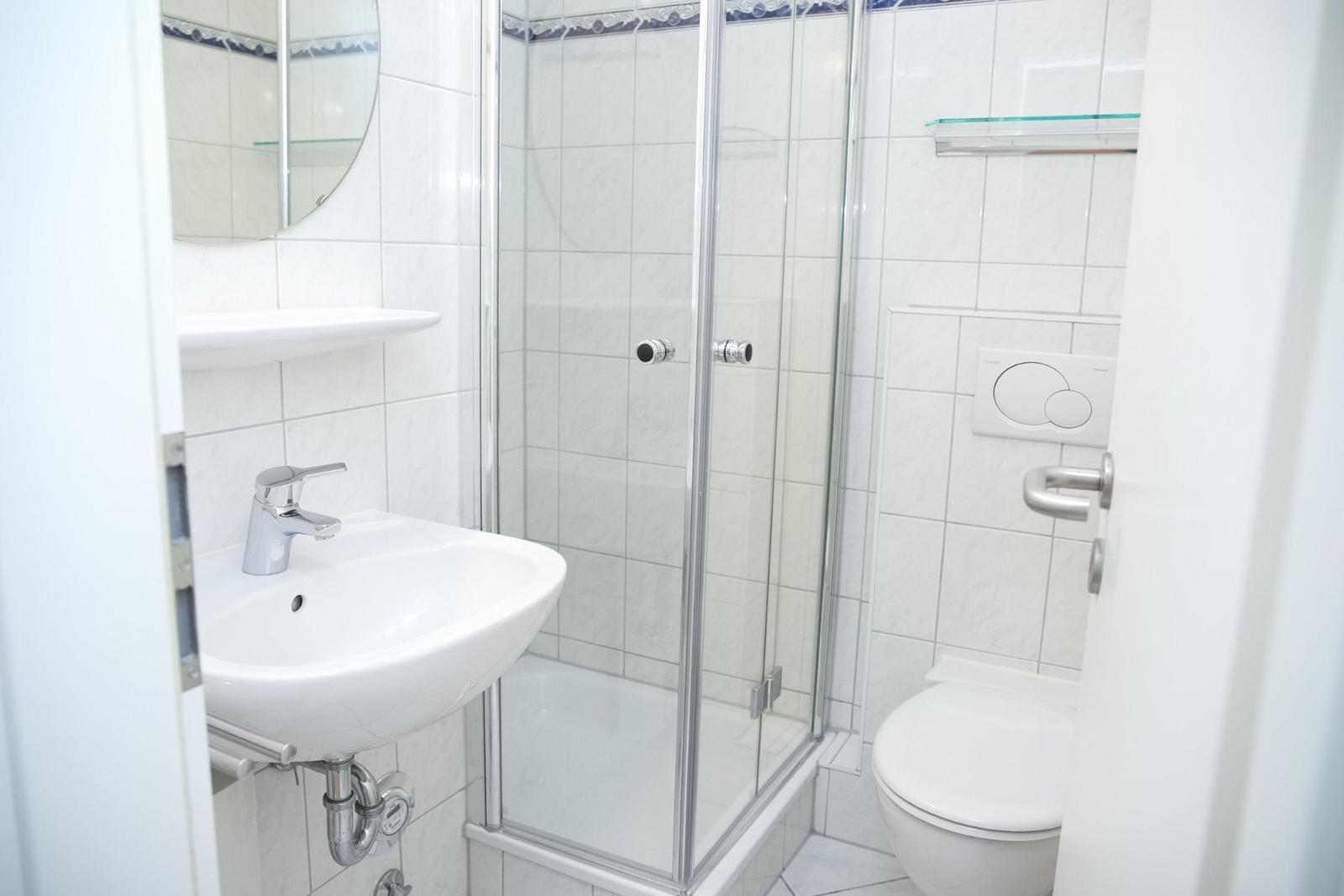 Badezimmer mit Dusche, Waschbecken und Toilette. Fliesenwand und Spiegel.