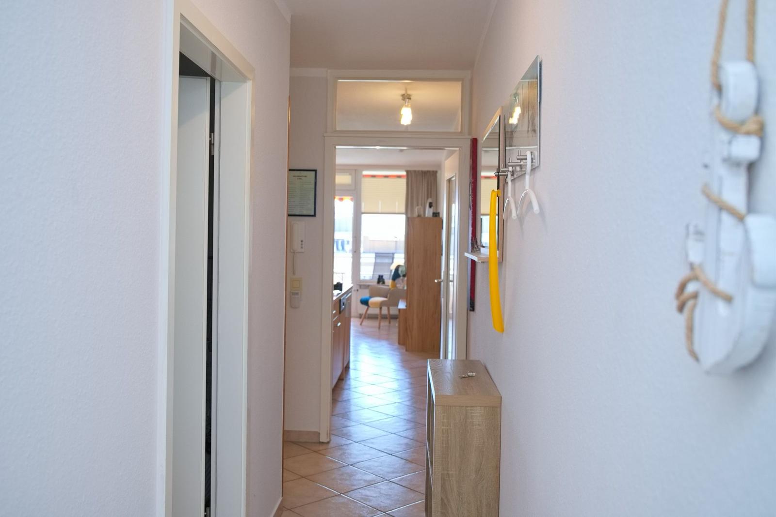 Flur mit Kleiderhaken, Schrank und Blick in Wohn- und Küchenbereich.