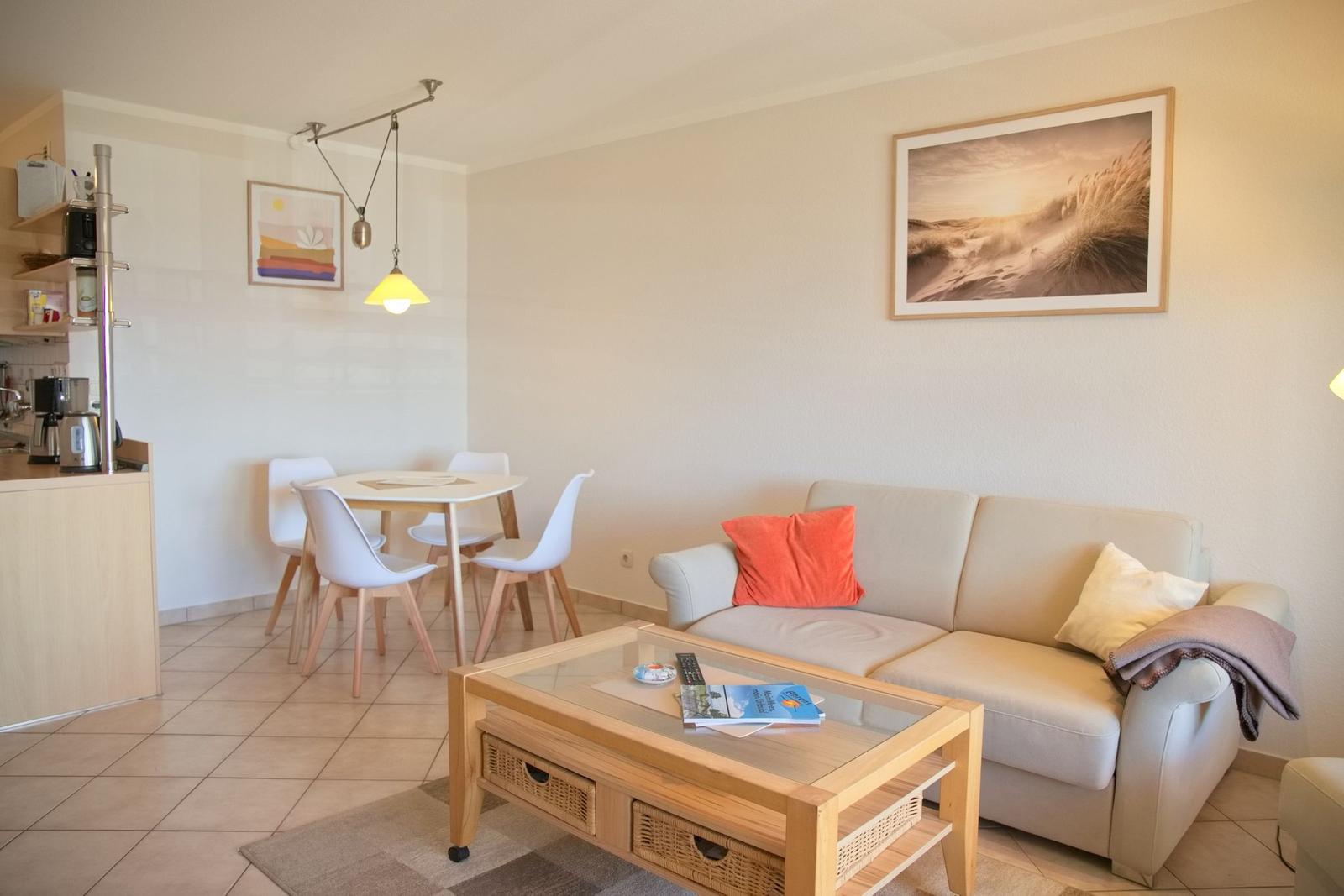 Wohnzimmer mit Sofa, Couchtisch und Essbereich. Wandbild und Beleuchtung sichtbar.