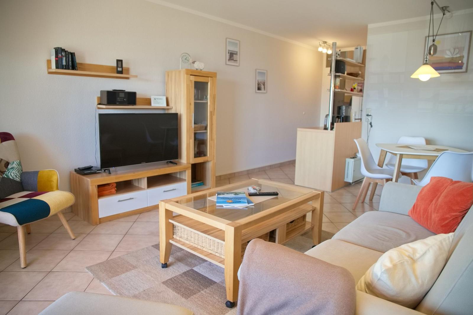 Wohnzimmer mit Sofa, Couchtisch und Fernseher. Essbereich mit Tisch und Stühlen im Hintergrund.