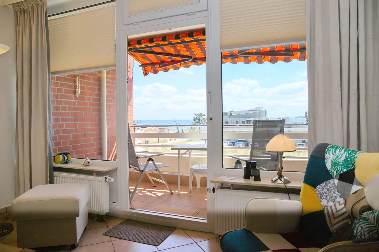 Wohnraum mit Blick auf Balkon und Meeresblick. Balkon mit Tisch, Stühlen und Markise.