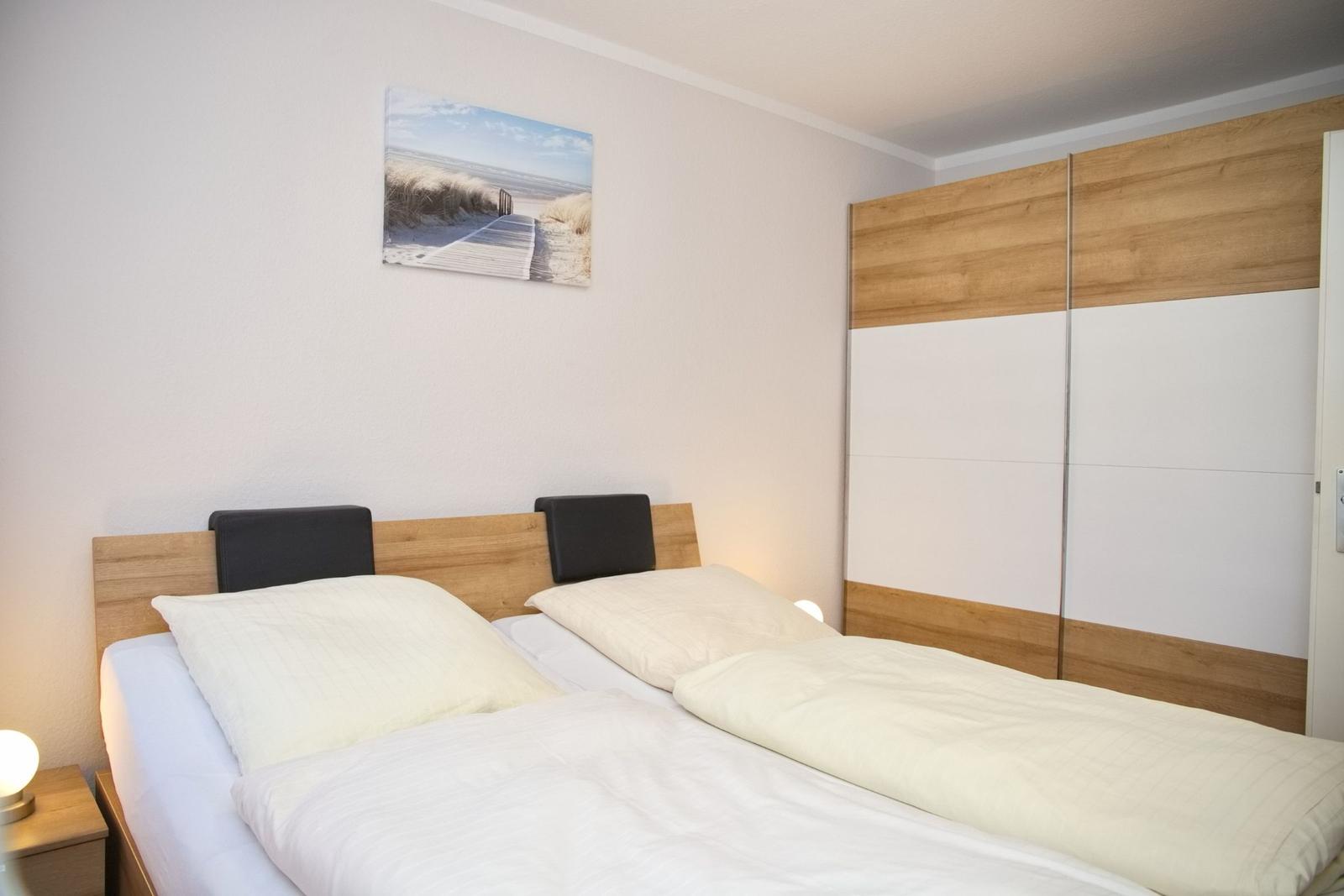 Schlafzimmer mit Doppelbett, Holzschrank und Wandbild.