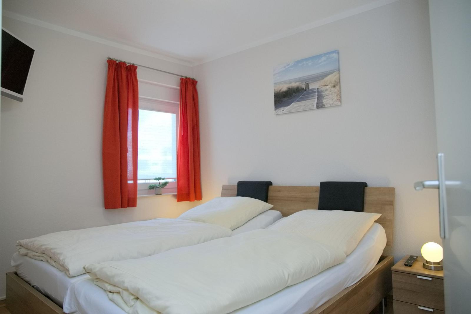 Schlafzimmer mit Doppelbett, roten Vorhängen und Wandbild.