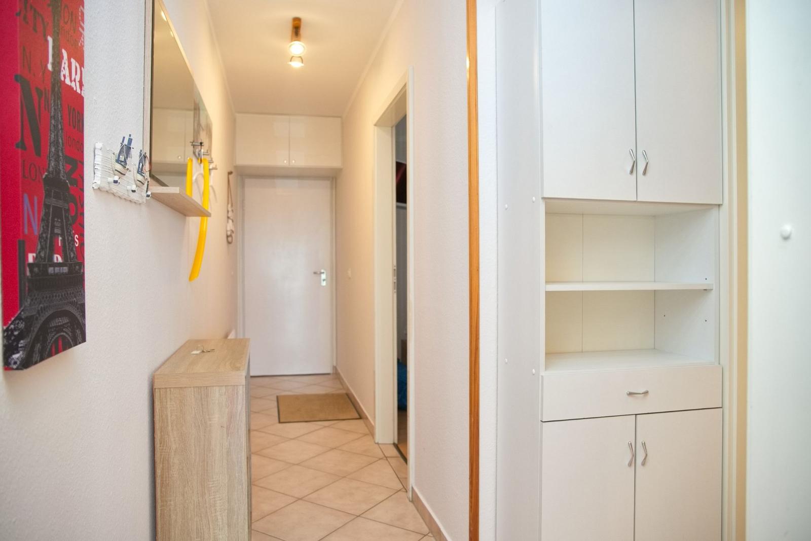 Flur mit weißen Schränken, Holzkonsole und Wandbild von Paris.