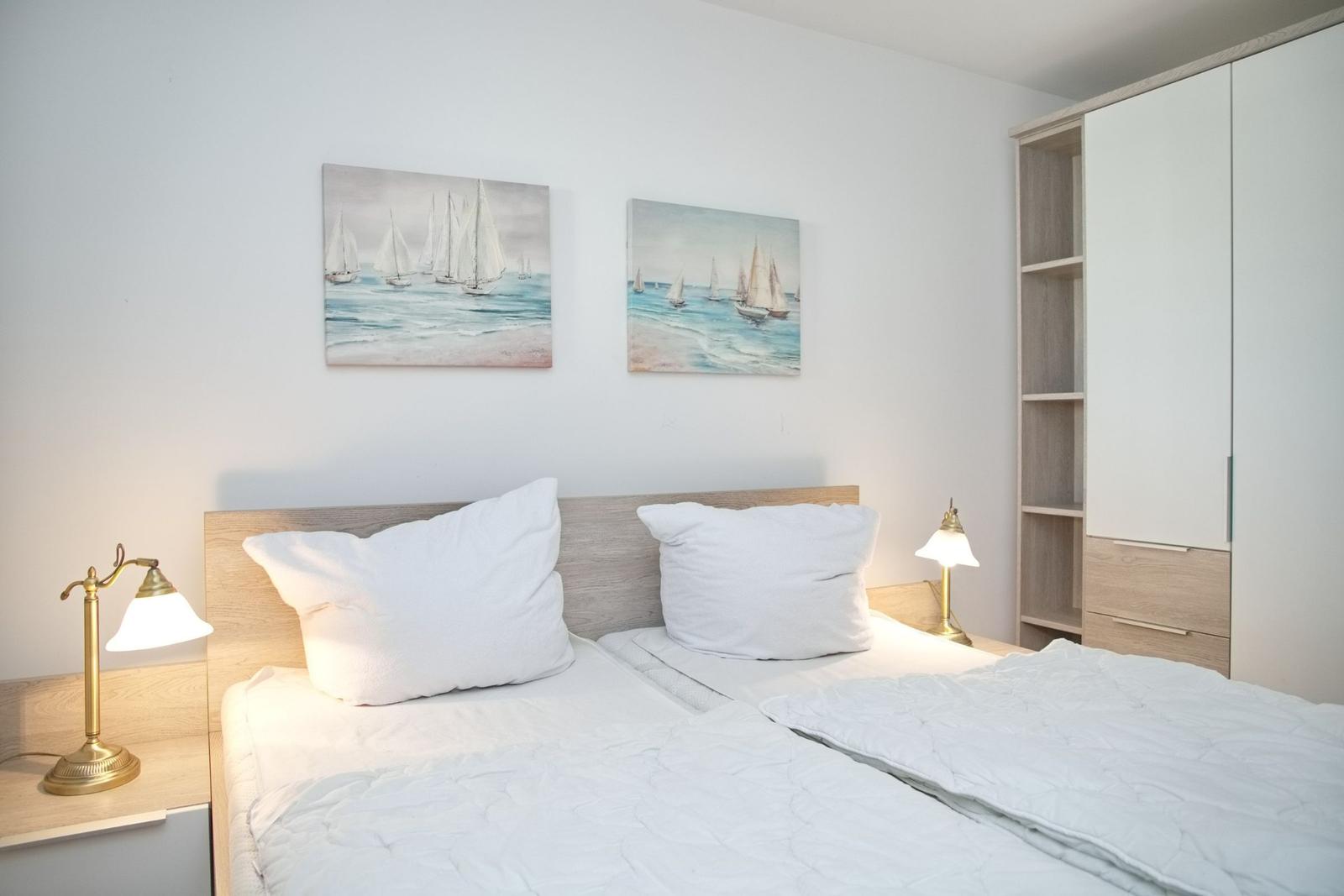 Schlafzimmer mit Doppelbett, zwei Nachttischen und Wandbildern mit Segelbooten.