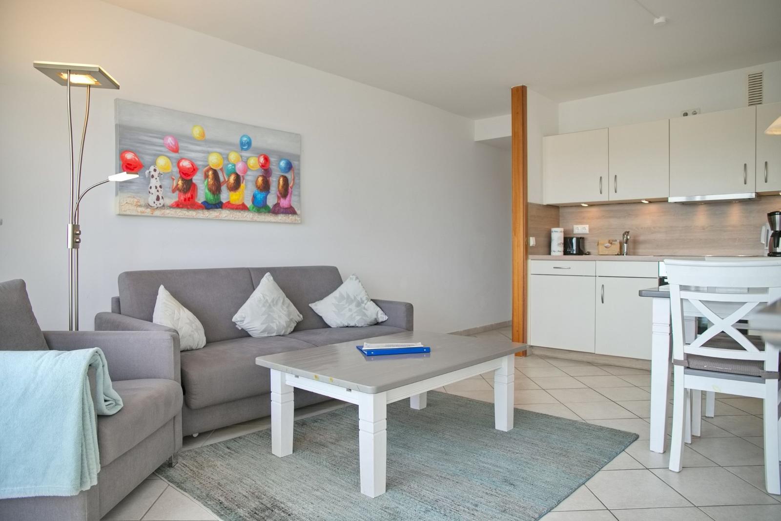 Wohnzimmer mit Sofa, Couchtisch und Küche im Hintergrund.