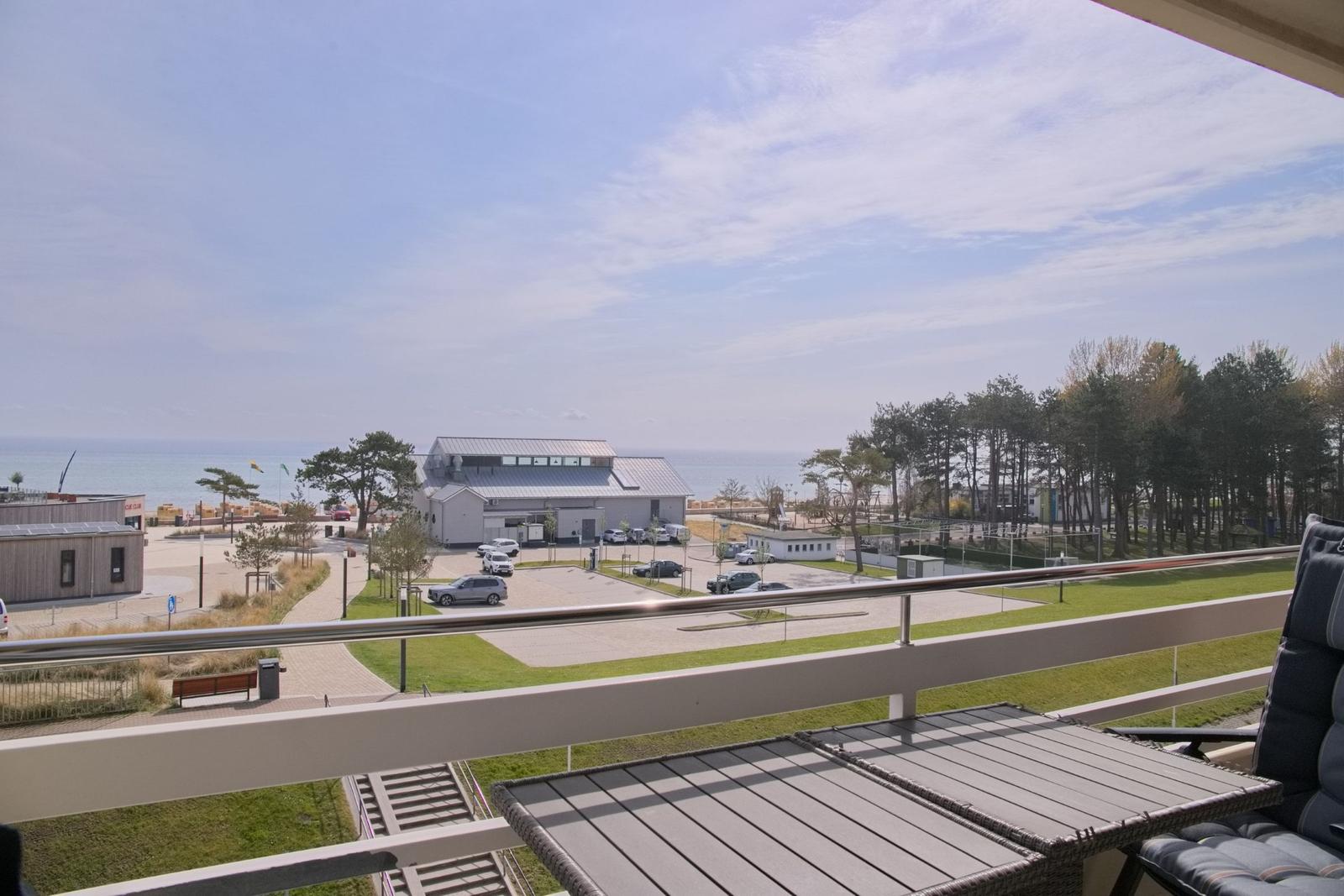Balkon mit Sitzgelegenheit und Blick auf Parkplatz und Strand.