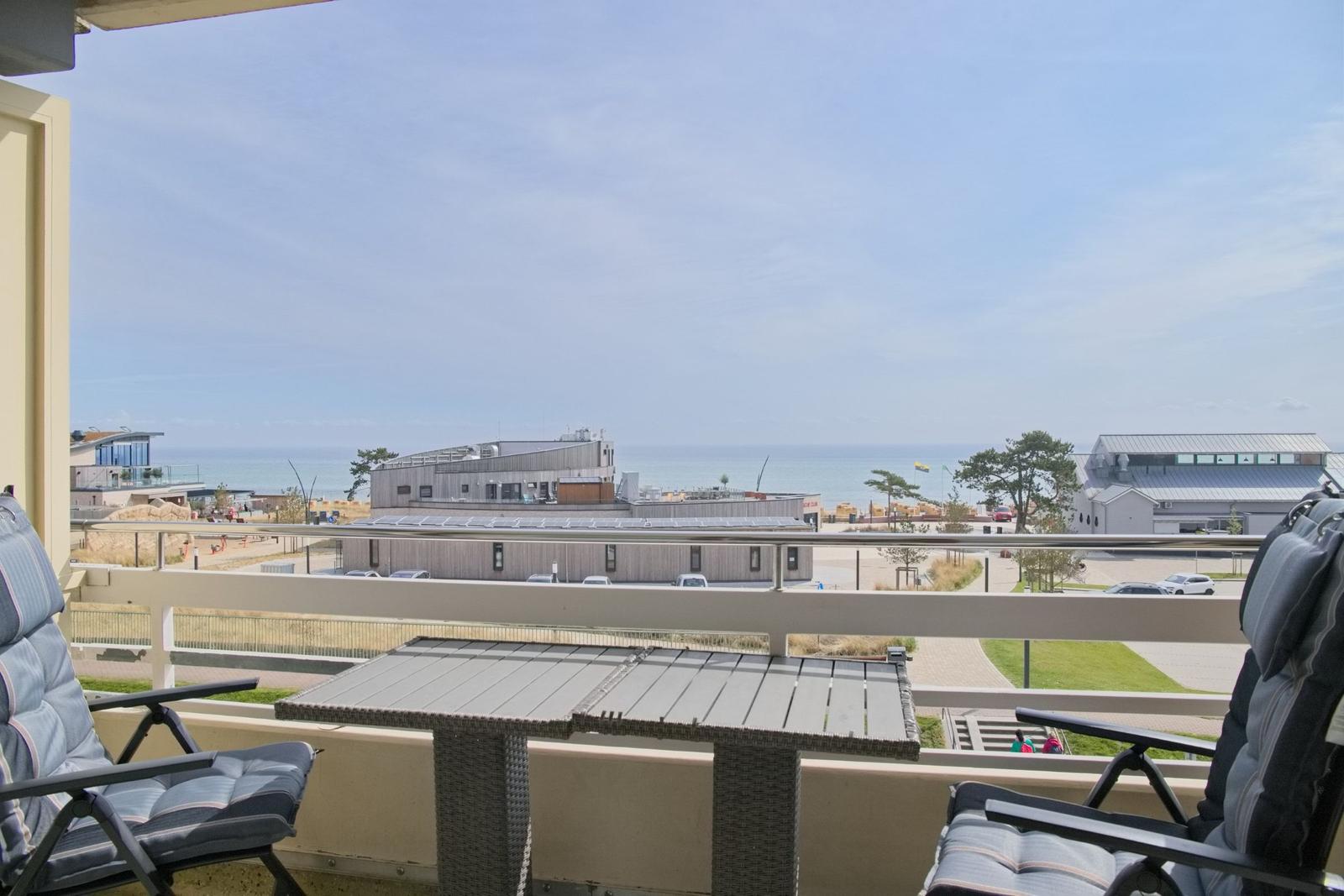 Terrasse mit Tisch und Stühlen, Blick auf Strand und Gebäude.
