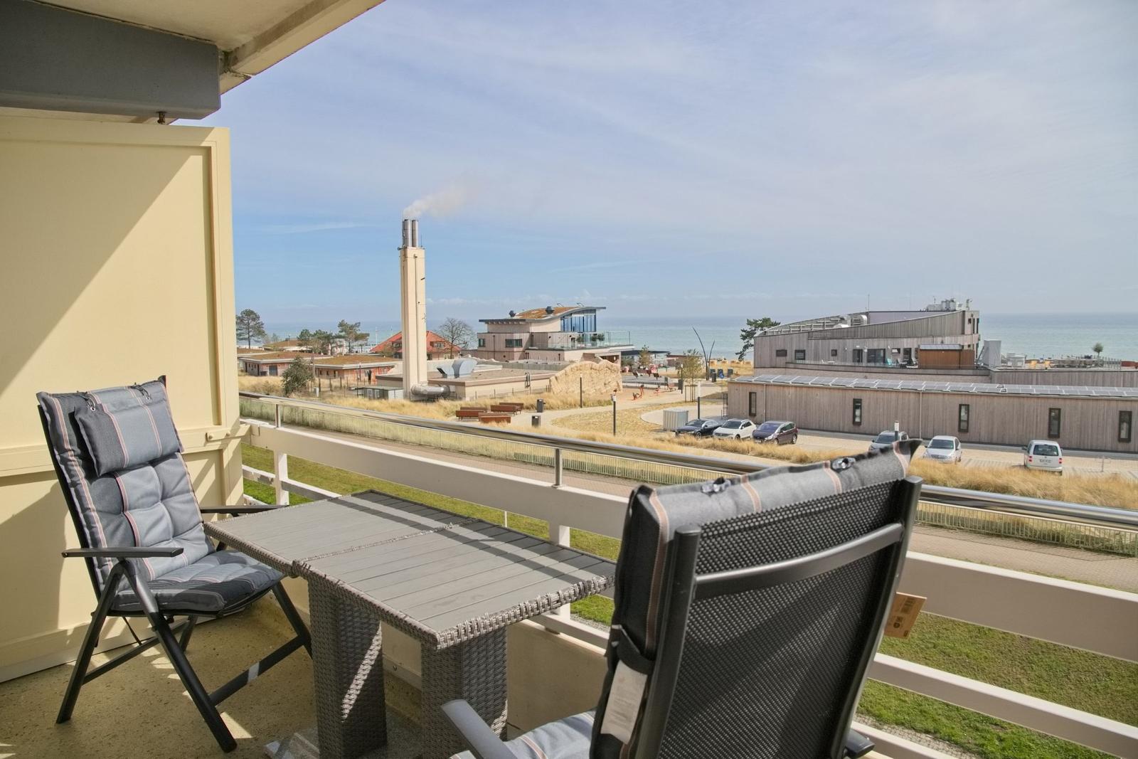 Terrasse mit zwei Liegestühlen und Tisch. Blick auf Gebäude und Meer.
