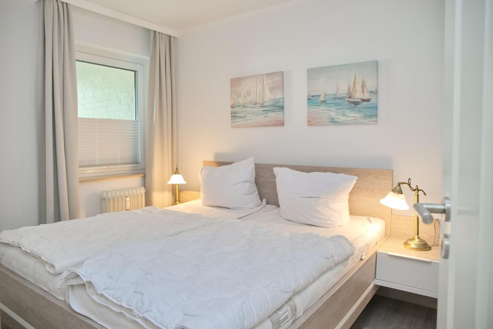 Ein Schlafzimmer mit Bett, Nachttischen und Wandbildern von Segelyachten.