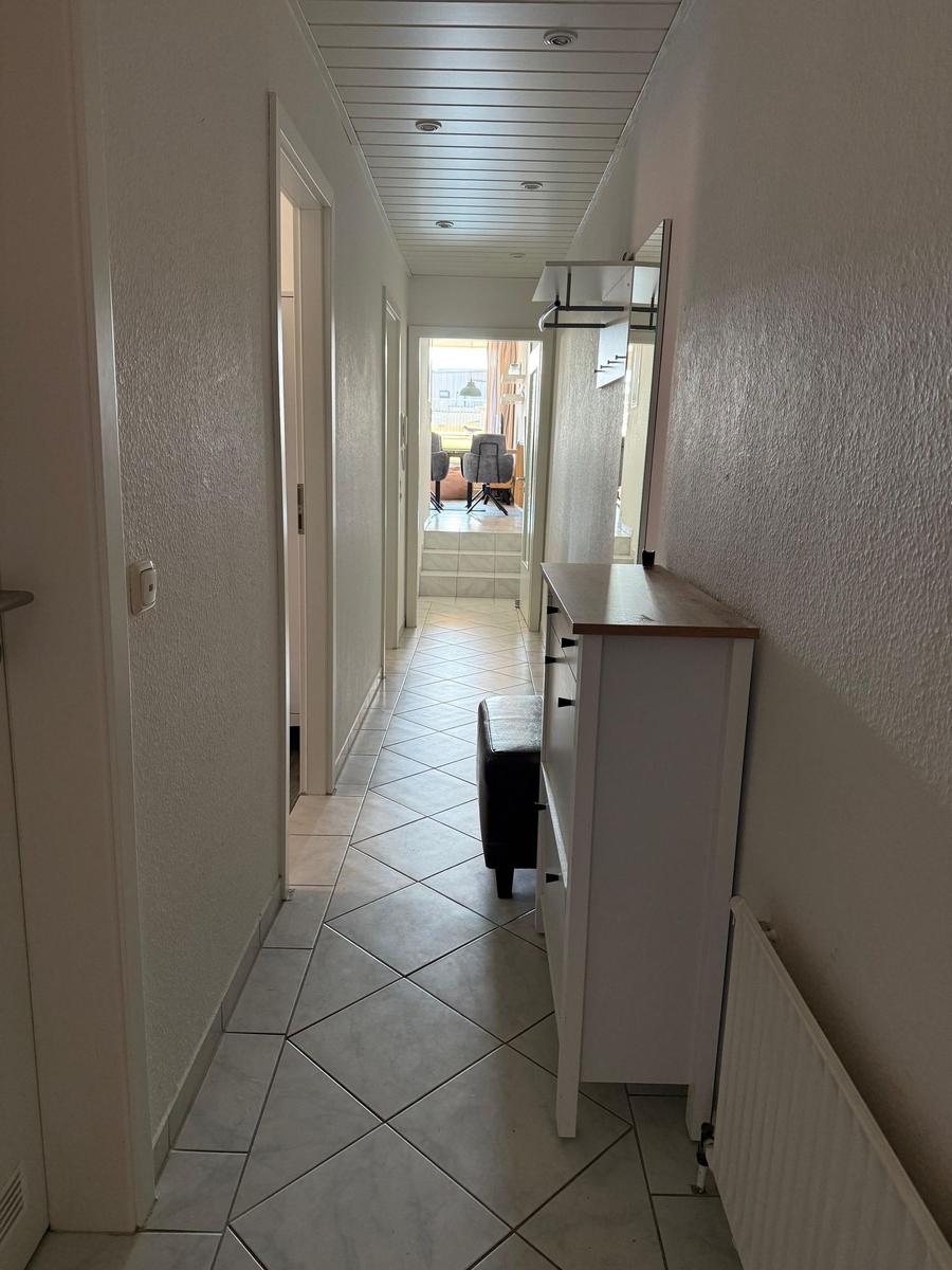 Flur mit weißen Wänden, gefliestem Boden und Schrank. Durchgang zum Essbereich.