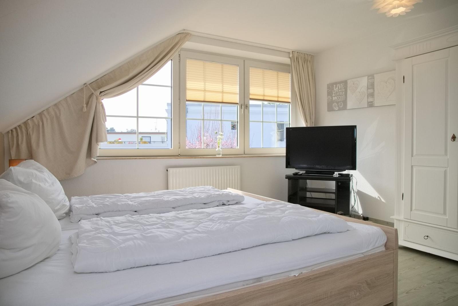 Schlafzimmer mit Doppelbett, Fenster und TV.