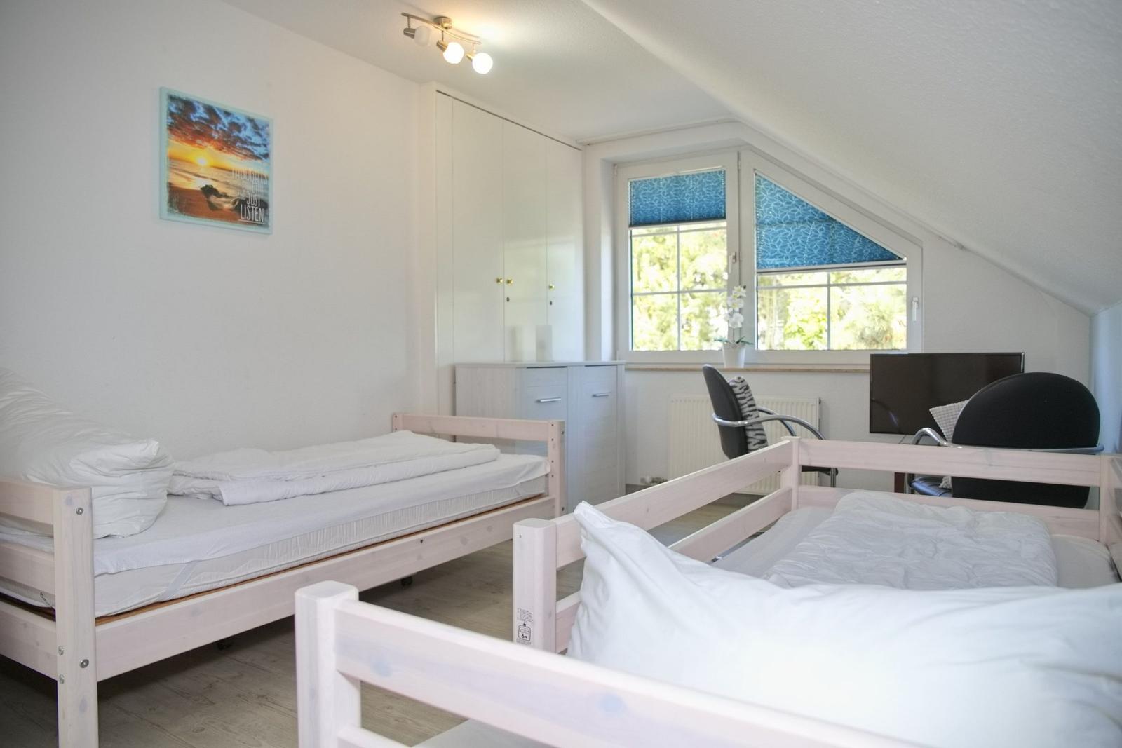 Zimmer mit zwei Betten, Schreibtisch und Fenster mit Blick auf Grün.