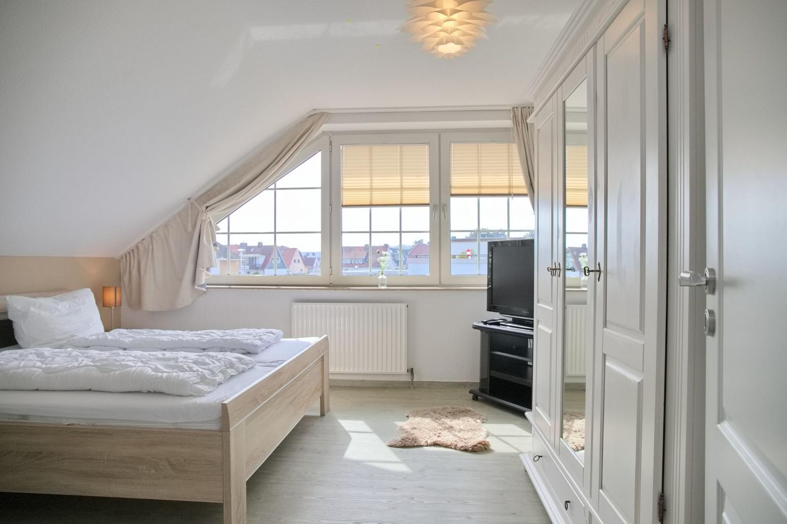 Schlafzimmer mit Dachschräge, Bett, Fenster und Kleiderschrank.