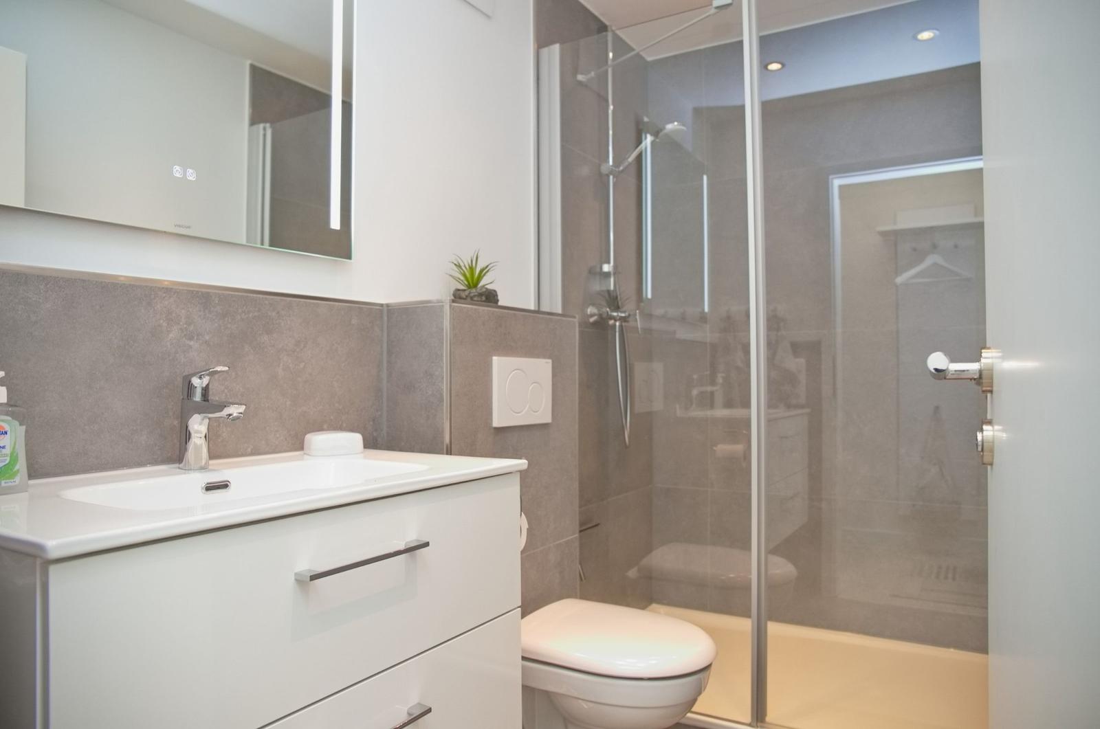 Badezimmer mit Waschbecken, Spiegel, Dusche und Toilette.