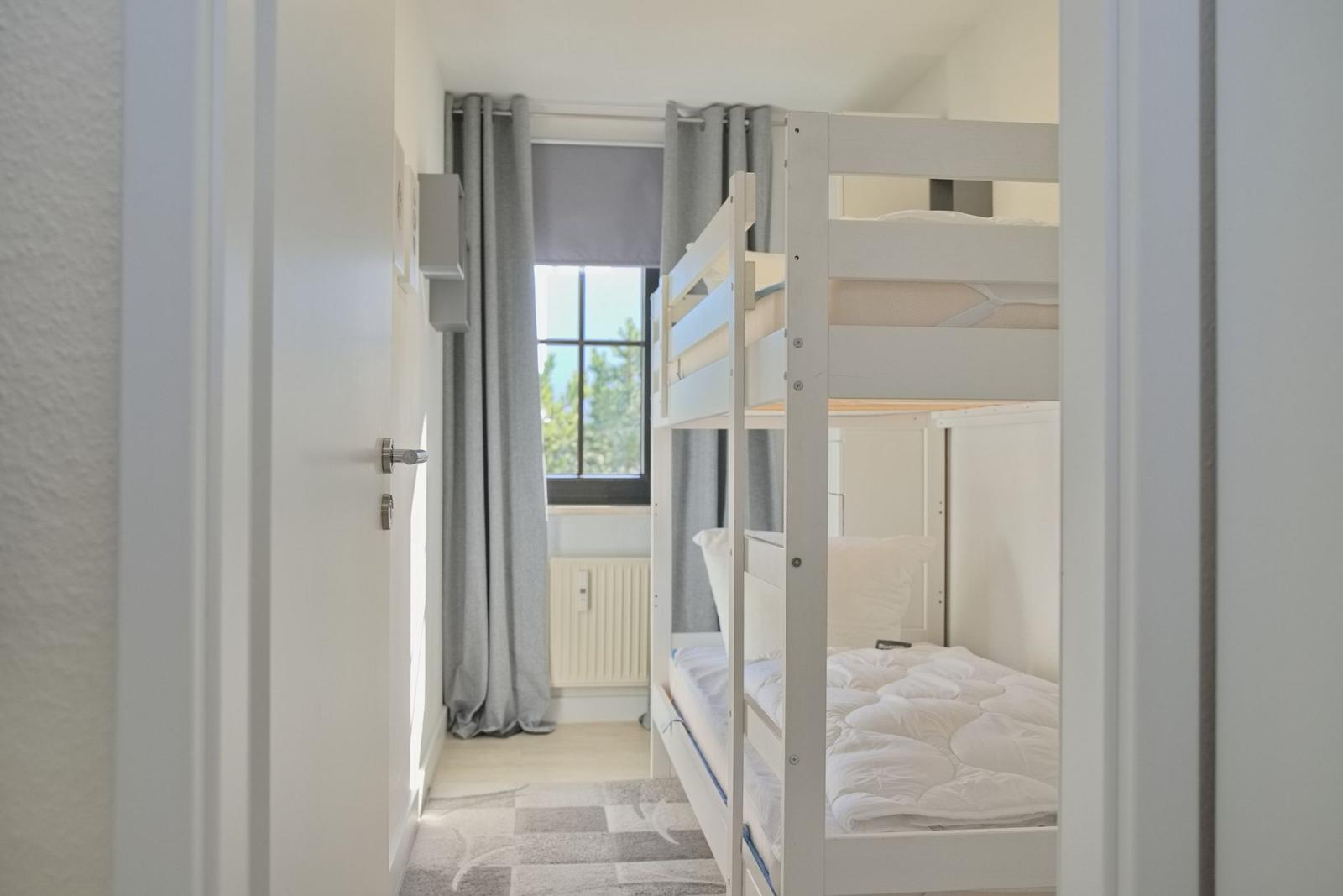 Zimmer mit Doppelstockbett, Fenster und grauen Vorhängen.