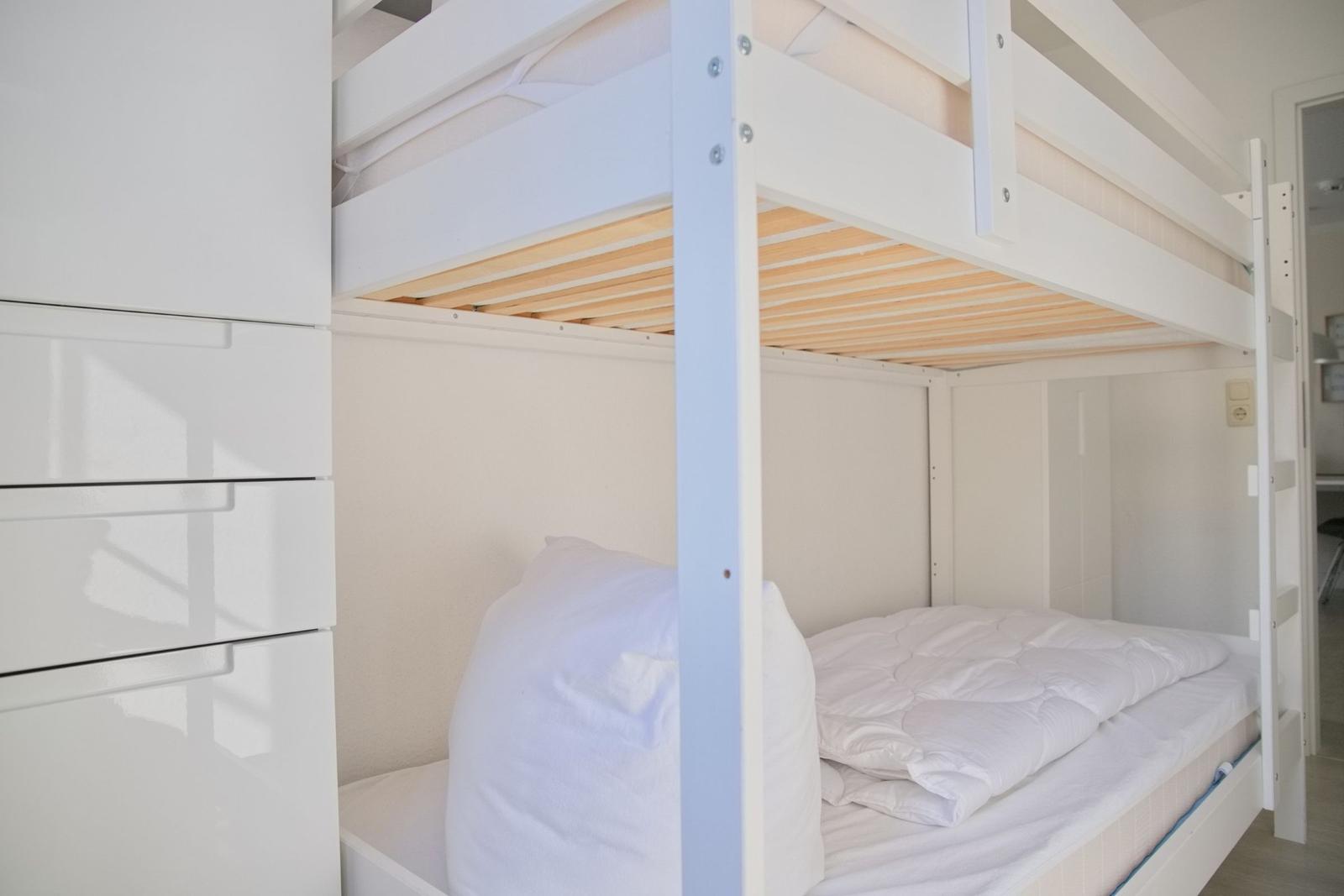 Doppelbett mit Matratze und Bettwäsche. Links steht ein weißer Schrank.