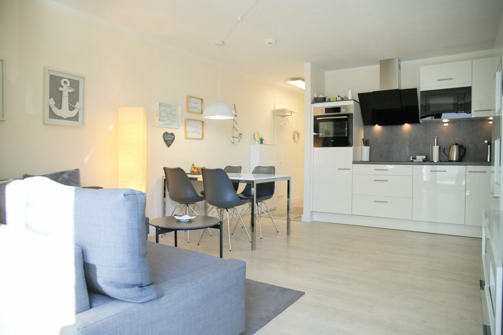 Wohn- und Essbereich mit Küchenzeile. Sofa, Tisch und Stühle sind sichtbar.