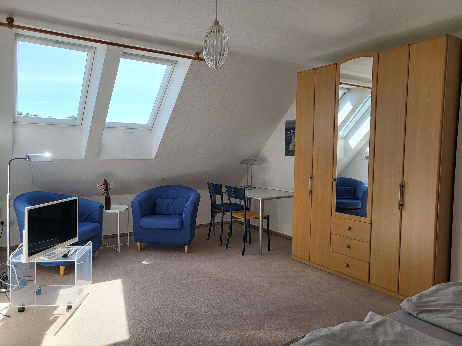 Zimmer mit Dachfenstern, blauen Sesseln, Schreibtisch und Kleiderschrank.