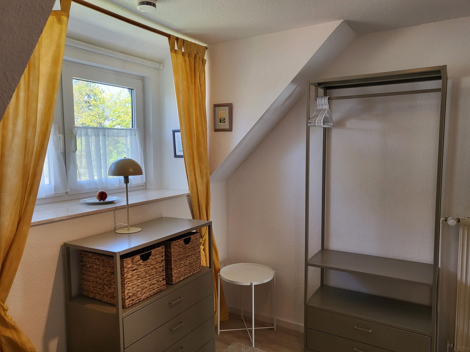 Schlafzimmer mit Dachschrägen, Fenster, Gardinen, Schrank und Nachttisch.