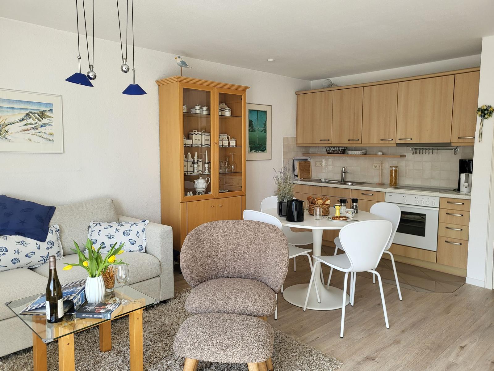 Wohnzimmer mit Essbereich und Küche. Holzmöbel, Tisch mit Stühlen, Sofa und Küchenzeile.