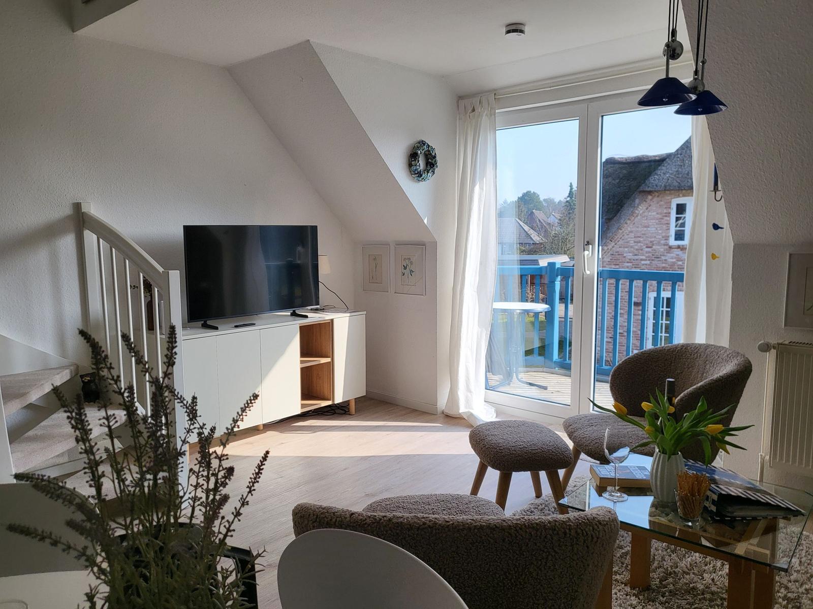 Wohnzimmer mit TV, Balkon und Sitzgelegenheiten. Dachgeschoss mit schrägen Wänden.