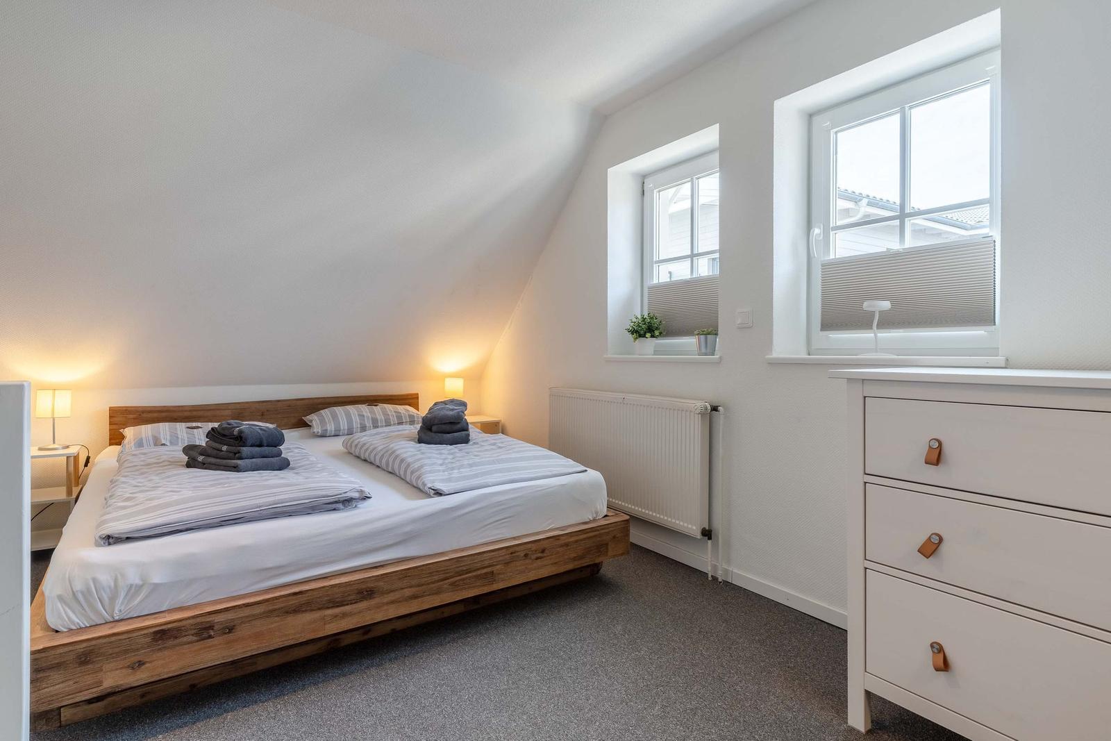 Schlafzimmer mit Doppelbett, zwei Fenstern und Schrank.