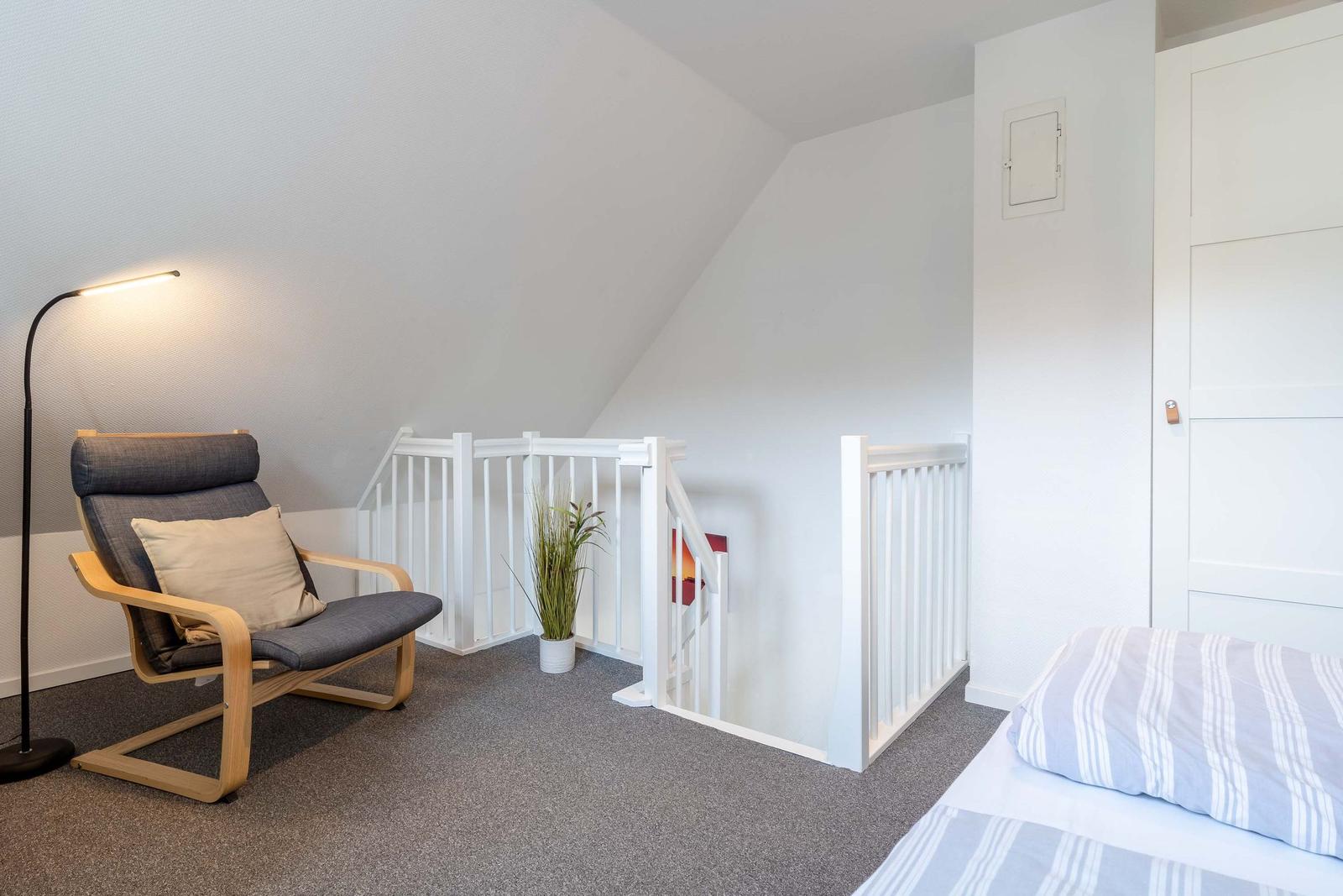 Zimmer mit Bett, Sessel und Treppe mit Geländer.