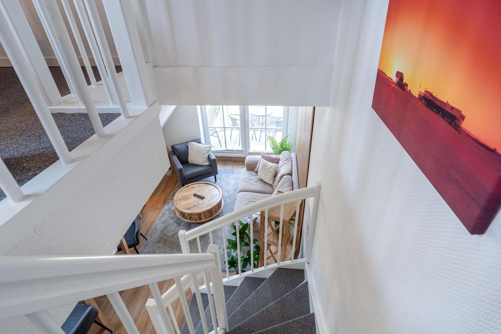 Von der Treppe aus Blick auf Wohnbereich mit Sofa, Sessel und Terrassentür.