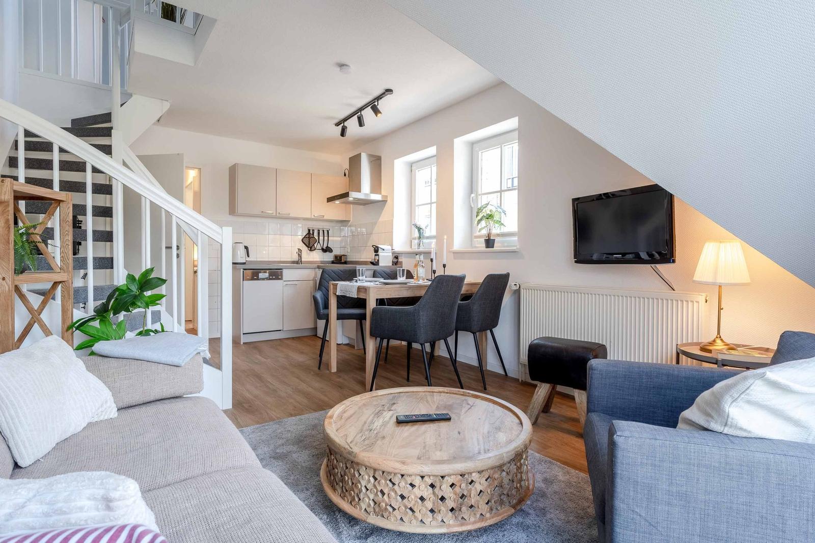 Wohnzimmer mit Sofa, Couchtisch und TV. Küche und Essbereich im Hintergrund.