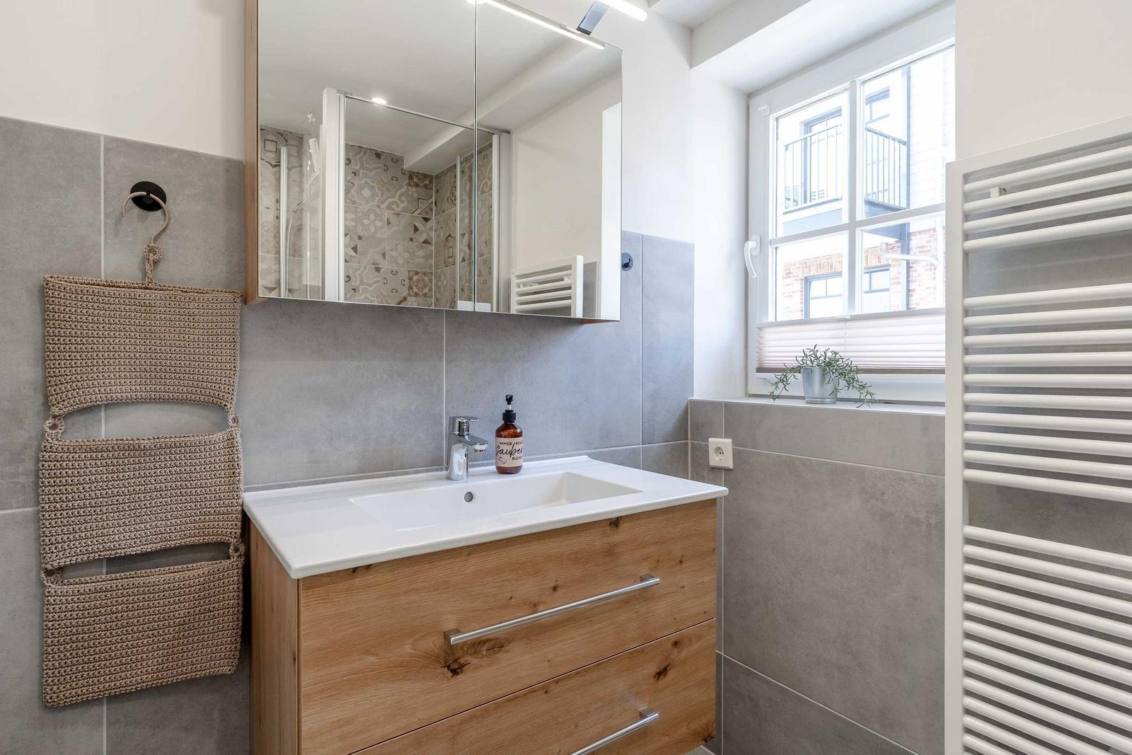 Bad mit Waschbecken, Spiegelschrank und Fenster mit Pflanze.