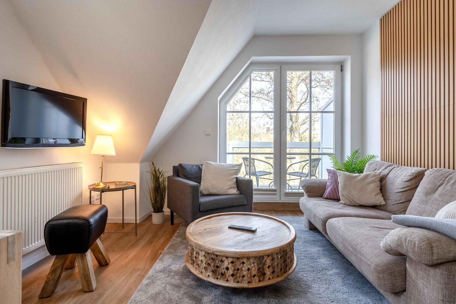 Wohnzimmer mit Sofa, Sessel, runden Tisch und TV an der Wand.