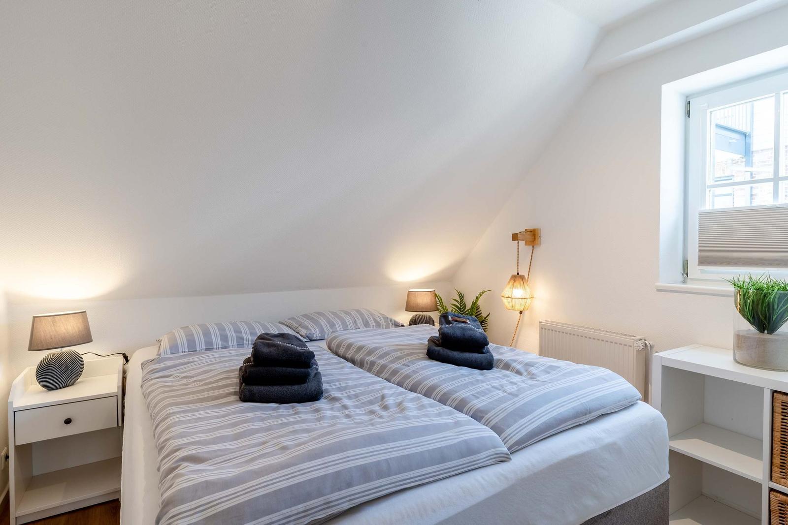 Schlafzimmer mit Doppelbett, zwei Nachttischen und Fenster mit Pflanze.